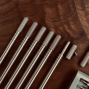 May include: A set of eight silver-toned metal screwdrivers with textured handles. The screwdrivers are laid out on a wooden surface.