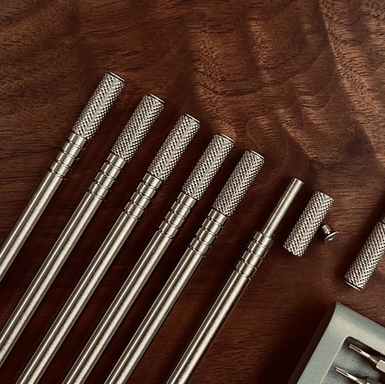 May include: A set of eight silver-toned metal screwdrivers with textured handles. The screwdrivers are laid out on a wooden surface.