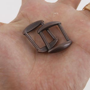 May include: Two antique bronze metal slider buckles. The buckles are rectangular with rounded edges and have a smooth, polished finish.