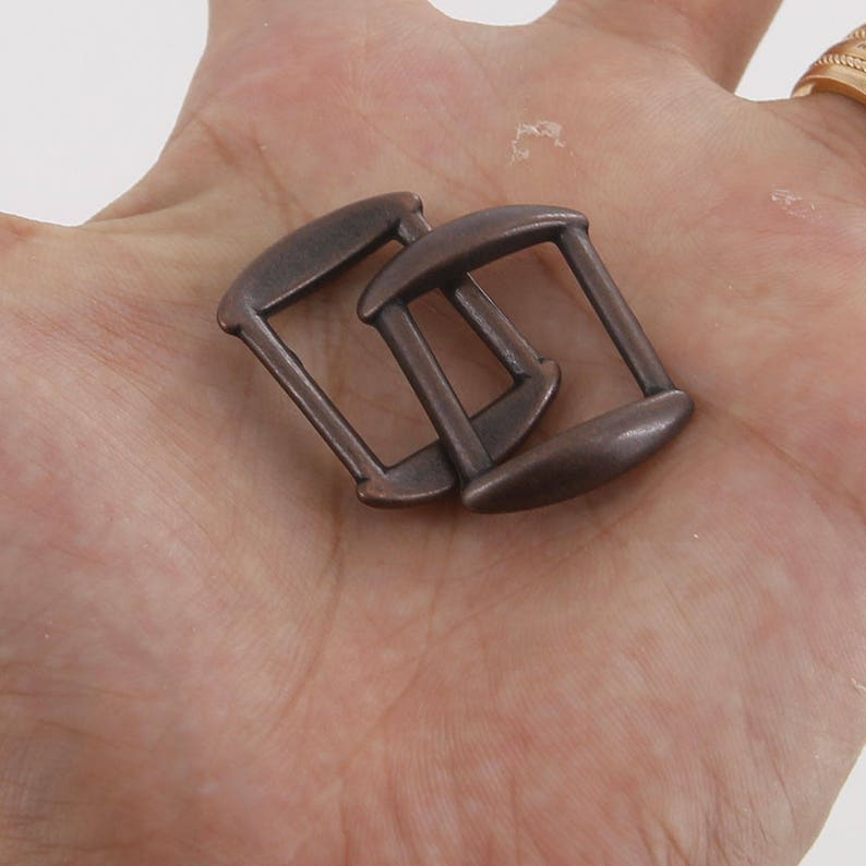 May include: Two antique bronze metal slider buckles. The buckles are rectangular with rounded edges and have a smooth, polished finish.
