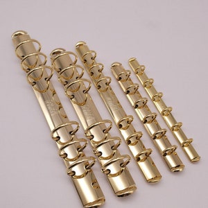 May include: Five gold metal binder rings of different sizes. The rings are all the same design, with a smooth, polished finish.
