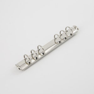 Könnte beinhalten: Silberne Ringbuchringe mit fünf Löchern. Die Ringe sind an einer Metallstange befestigt.