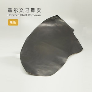 Può includere: Un pezzo di pelle Horween Shell Cordovan nero. La pelle è liscia e ha una leggera lucentezza. Il testo "Horween Shell Cordovan" è scritto in nero sopra la pelle. Il testo "黑色" è scritto in giallo sotto la pelle.