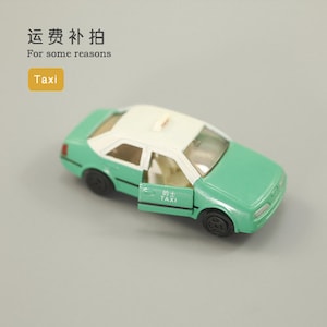 Könnte beinhalten: Ein grünes und weißes Spielzeugtaxi mit geöffneter Tür. Das Taxi hat schwarze Räder und ein weißes Dachschild. Das Wort "Taxi" steht in einem gelben Feld. Der Text "For some reasons" steht über dem Taxi.