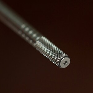 May include: A close-up of a silver metal tool with a hexagonal head and a textured grip.