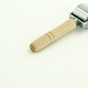 May include: A silver and wooden roller tool with a wooden handle. The roller is made of metal and has a smooth surface. The handle is made of wood and has a natural finish.