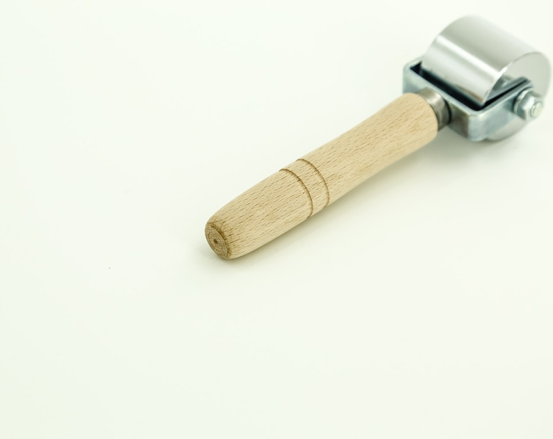 May include: A silver and wooden roller tool with a wooden handle. The roller is made of metal and has a smooth surface. The handle is made of wood and has a natural finish.