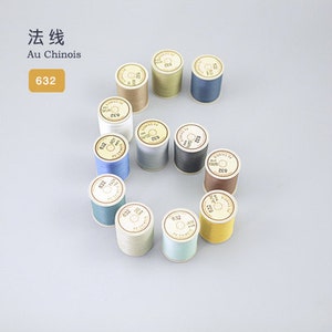 Puede incluir: Una colección de 12 carretes de hilo Au Chinois en varios colores, incluyendo beige, marrón, gris, azul y amarillo. Cada carrete está etiquetado con el número "632".