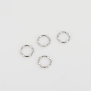 Puede incluir: Cuatro anillos de salto plateados, cada uno con una forma circular lisa. Estos anillos se utilizan comúnmente en la fabricación de joyas y la artesanía.