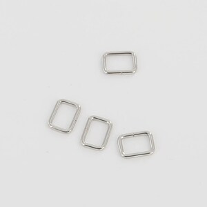 May include: Four silver rectangular metal buckles. The buckles are evenly spaced against a white background. The buckles are likely used for straps or belts.