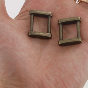 K&ouml;nnte beinhalten: Zwei antike goldfarbene Metall-Schiebeschlie&szlig;en. Die Schlie&szlig;en sind rechteckig mit einer quadratischen &Ouml;ffnung in der Mitte. Die Schlie&szlig;en sind etwa 2,5 cm lang und 1,25 cm breit.