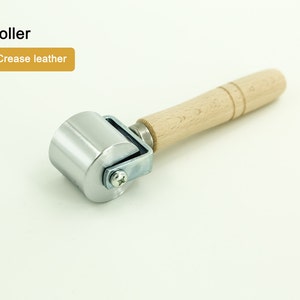 May include: A silver roller with a wooden handle. The roller is used to crease leather.