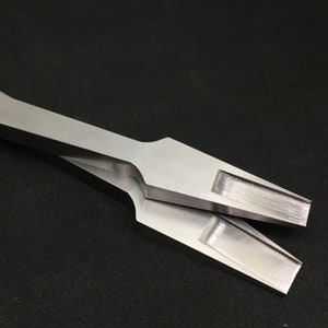 Op de afbeelding: Twee zilveren metalen gereedschappen met een plat, rechthoekig blad en een puntige punt. De gereedschappen zijn op elkaar gestapeld.