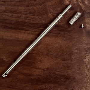 May include: A silver metal tool with a threaded shaft and a small, knurled knob. The tool is disassembled and laid out on a wooden surface.