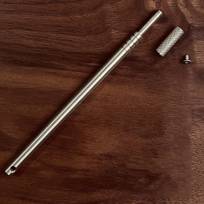 May include: A silver metal tool with a threaded shaft and a small, knurled knob. The tool is disassembled and laid out on a wooden surface.