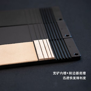 Puede incluir: Una piedra de afilar de cuero negro con una superficie texturizada y una tira de cuero blanco para afilar. La piedra de afilar está diseñada para afilar cuchillos y otras herramientas.