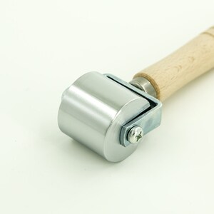 May include: A silver roller with a wooden handle. The roller is used for smoothing out surfaces, such as fabric or paper.