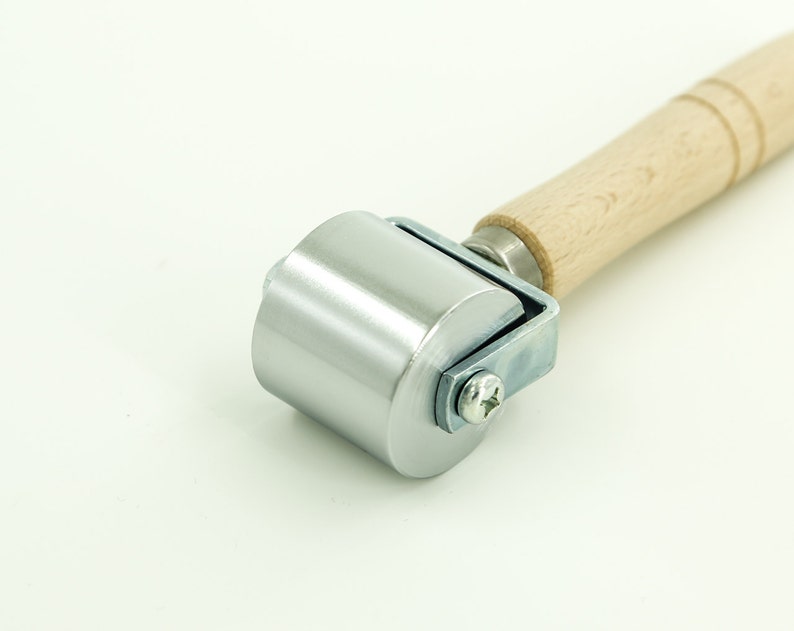 May include: A silver roller with a wooden handle. The roller is used for smoothing out surfaces, such as fabric or paper.
