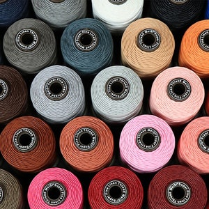 May include: A collection of spools of super fine linen thread in various colors, including gray, blue, brown, pink, red, and orange. Each spool has a label that reads "Super Fine Linen Thread".