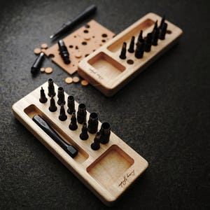 May include: A wooden tool organizer with a variety of leather hole punches and a small hammer. The organizer has a compartment for storing the tools and a label that says "Hand Made".