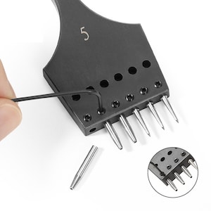 Puede incluir: Una herramienta de punzonado de cuero de metal negro con el número "5" en la parte superior. La herramienta tiene siete punzones de metal que son extraíbles. Los punzones están dispuestos en una fila y son de diferentes tamaños. Una pequeña llave inglesa negra se utiliza para quitar los punzones. Un punzón está sobre la superficie blanca.