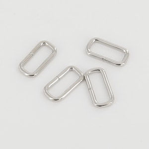 May include: Four silver metal rectangular rings, also known as D-rings, are shown against a white background. These rings are commonly used for attaching straps, handles, or other accessories to bags, belts, or other items.