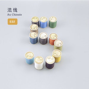 Puede incluir: Una colección de 10 carretes de hilo en varios colores, incluyendo beige, azul, verde, marrón, naranja, amarillo y blanco. Los carretes están etiquetados con el número "532" y el texto "Au Chinois".