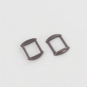 May include: Two antique gold-toned metal slider buckles. The buckles are rectangular with rounded edges and have a smooth finish.