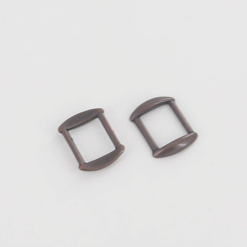 May include: Two antique gold-toned metal slider buckles. The buckles are rectangular with rounded edges and have a smooth finish.
