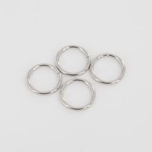 Puede incluir: Cuatro anillos de metal plateado, cada uno con forma circular y un acabado liso y pulido.