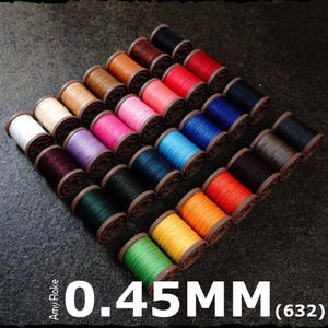 Pode incluir: Uma coleção de carretéis de fio de 0,45 mm em várias cores, incluindo vermelho, azul, verde, amarelo e preto. Os carretéis estão dispostos em um padrão circular sobre uma superfície escura.