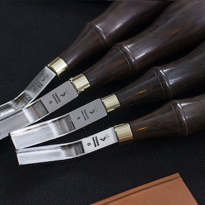 Puede incluir: Primer plano de un juego de herramientas para trabajar el cuero. Las herramientas tienen mangos de madera marrón oscuro con collares de latón y hojas plateadas brillantes. Las hojas están marcadas con el texto "Yorkshire hand made" y números.