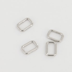 May include: Four silver metal D-rings, also known as D rings or D-shaped rings, are shown against a white background. These rings are commonly used in crafting, jewellery making, and other DIY projects.