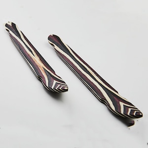 May include: Two wooden guitar picks with a black, white, and red striped pattern. The picks are shaped like a teardrop with a pointed tip.