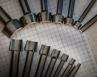 May include: A selection of dark metal leathercraft tools, each with a cylindrical handle and a curved, U-shaped cutting edge. The tools are arranged in a semi-circle on a grid background, likely a craft workspace.