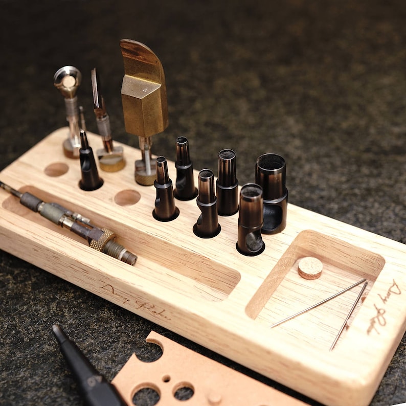 May include: A wooden tool organizer with a variety of leather crafting tools, including punches, awls, and a stitching tool. The organizer has a label that reads "Don't forget..."
