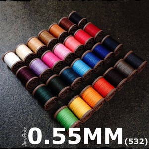 May include: A collection of 0.55mm waxed thread spools in various colours, including red, blue, green, yellow, and purple. The spools are arranged in a circular pattern on a dark surface.