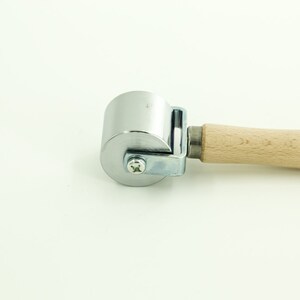 May include: A silver roller with a wooden handle. The roller is used for smoothing out surfaces.