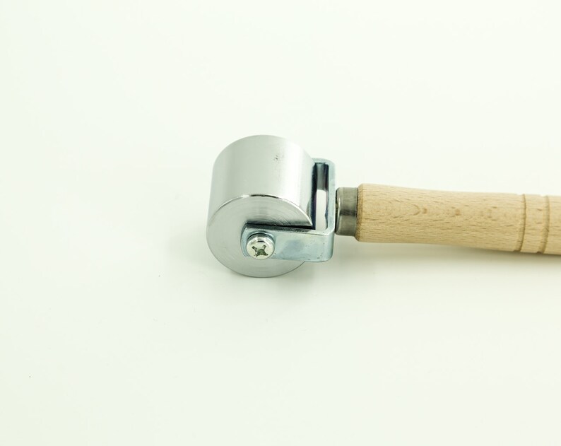 May include: A silver roller with a wooden handle. The roller is used for smoothing out surfaces.