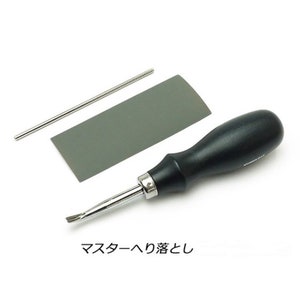 May include: A black handled tool with a silver blade for leather crafting. The tool is accompanied by a gray sharpening stone and a silver metal rod.