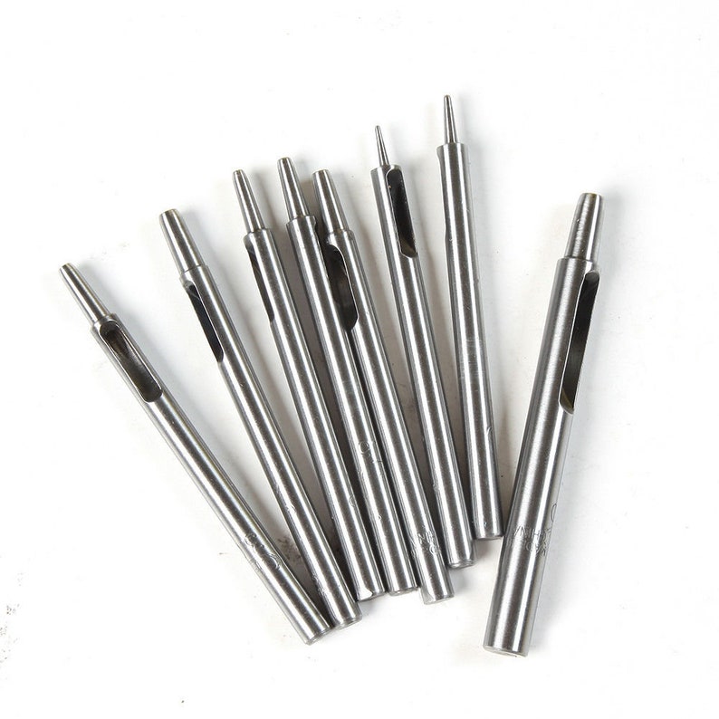 May include: A set of eight silver metal leather hole punches of varying sizes. The punches are arranged in a fan shape on a white background.