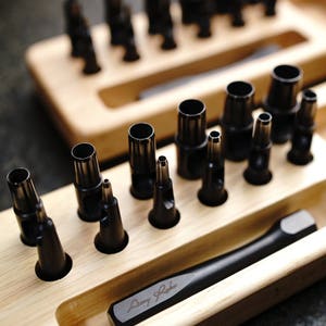 May include: A wooden tray with a set of black leather hole punches. The tray has a signature that reads "Danny Roberts".