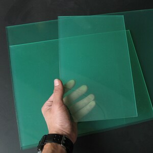 Peut inclure: Trois feuilles de plastique acrylique vert translucide. Les feuilles sont empil&eacute;es les unes sur les autres. Une main tient la feuille du dessus.