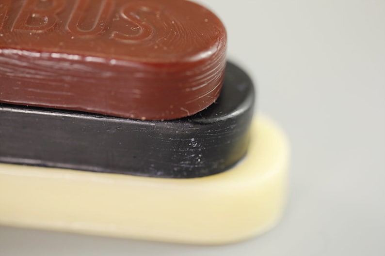 May include: Three oval-shaped blocks of wax stacked on top of each other. The top block is brown and has the word "BUS" embossed on it. The middle block is black, and the bottom block is white.