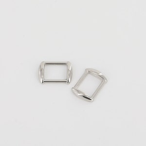 May include: Two silver-colored rectangular belt buckles with rounded edges are displayed against a white background. The buckles are made of a shiny metal and have a simple, minimalist design, suitable for various crafting projects.