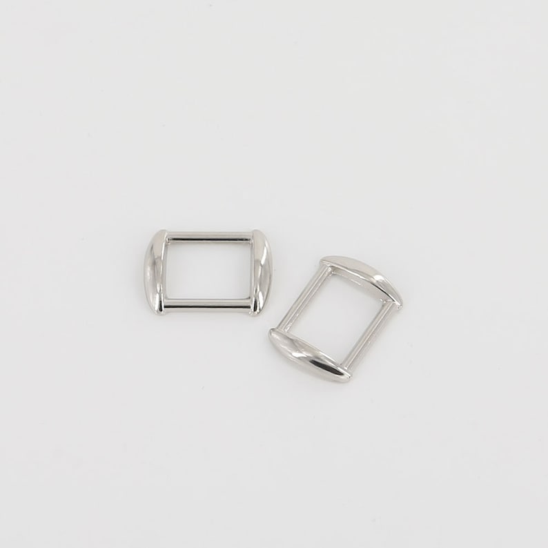 Puede incluir: Dos hebillas rectangulares plateadas con bordes redondeados sobre fondo blanco. Las hebillas, de metal brillante, presentan un dise&ntilde;o simple y minimalista. Ideales para diversos proyectos de manualidades.
