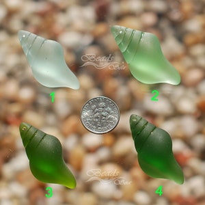 May include: Four sea glass shell beads in shades of green and blue. The beads are arranged in a circle around a UK ten pence coin. The beads are all about the size of a ten pence coin.