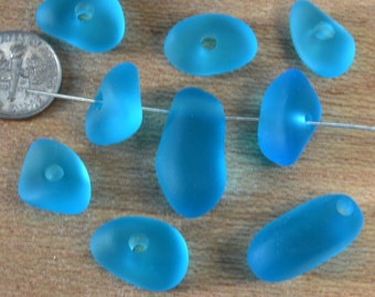 May include: A strand of eight turquoise sea glass beads with holes drilled through the center. The beads are various shapes and sizes, and are strung on a clear thread.