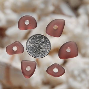 May include: Six mauve-colored glass beads with holes in the center. The beads are arranged in a circle around a US dime.