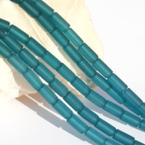 May include: Teal blue glass beads, frosted and cylindrical in shape. The beads are strung together in a long strand.